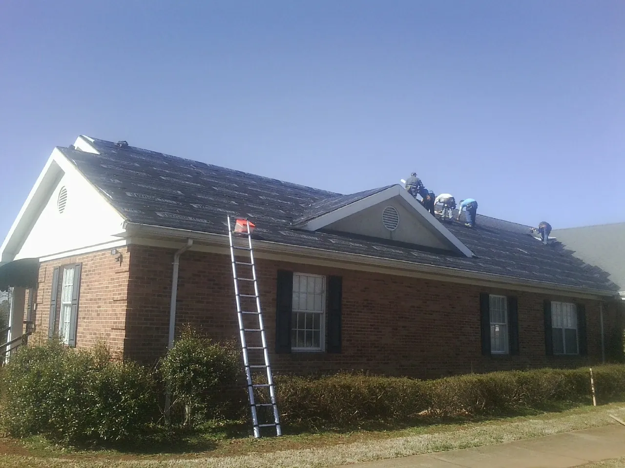 Crew tearing shingles off a brick ranch roof with a ladder set — Emergency Roof Repair work by our crew in Westmoreland