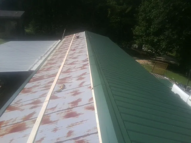 Old rusted panels beside newly installed green metal roofing — Wind Damage Roof Repair by Roofing Brothers in Westmoreland
