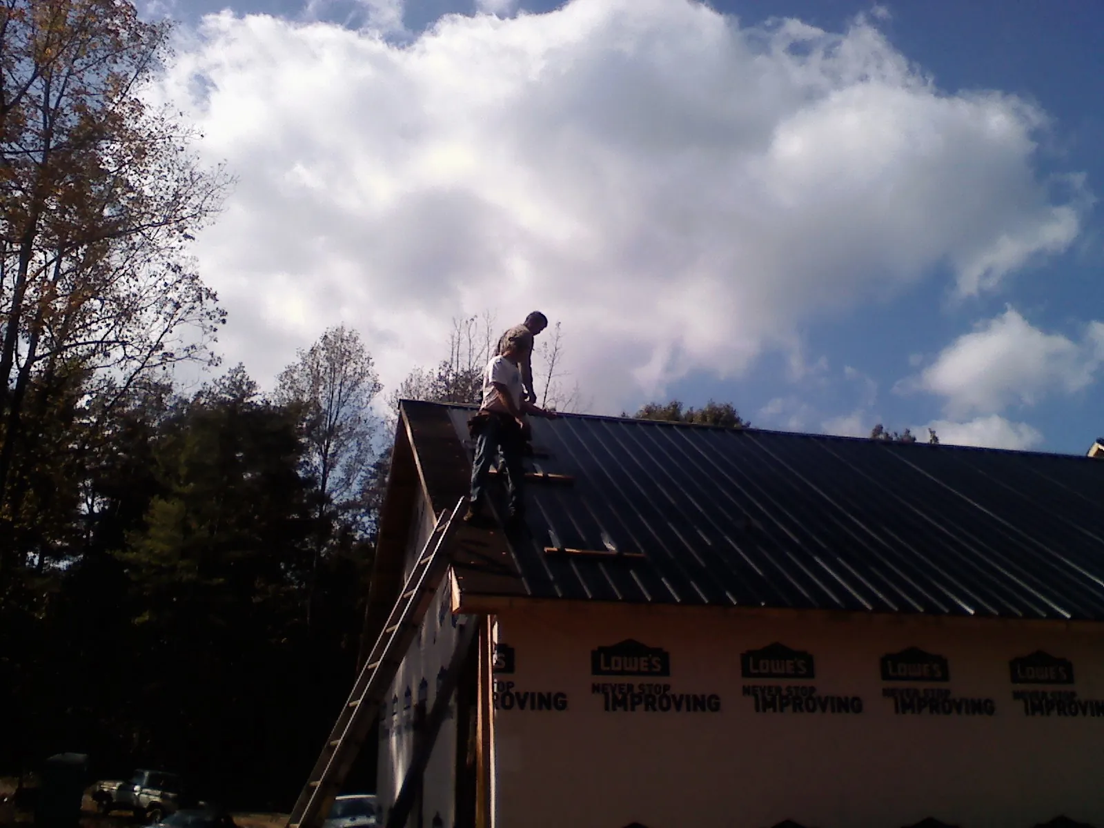 Roofer fastening dark metal panels high against a cloudy sky in Westmoreland